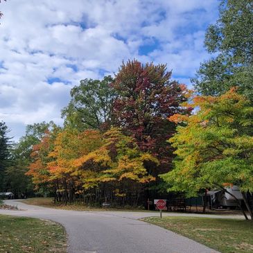 A scenic road surrounded by colorful autumn trees under a partly cloudy sky.