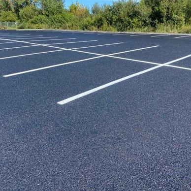 Empty freshly paved parking lot with white lines and trees in the background.