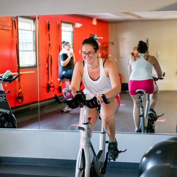 Women enjoying a spin class in a bright gym with red walls and mirrors.