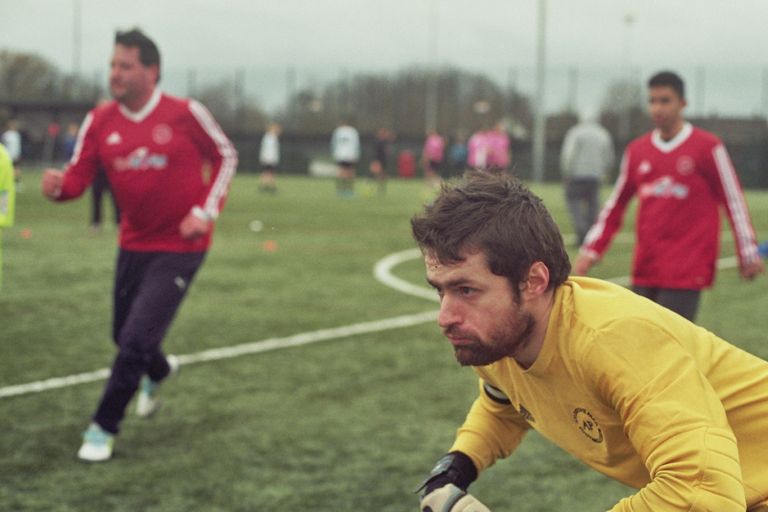The image shows a game of football on a 3G pitch, 3 players are awaiting a corner kick to be taken