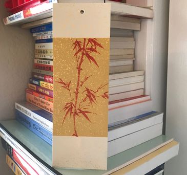 Bookmark with red bamboo design against a bookshelf background.
