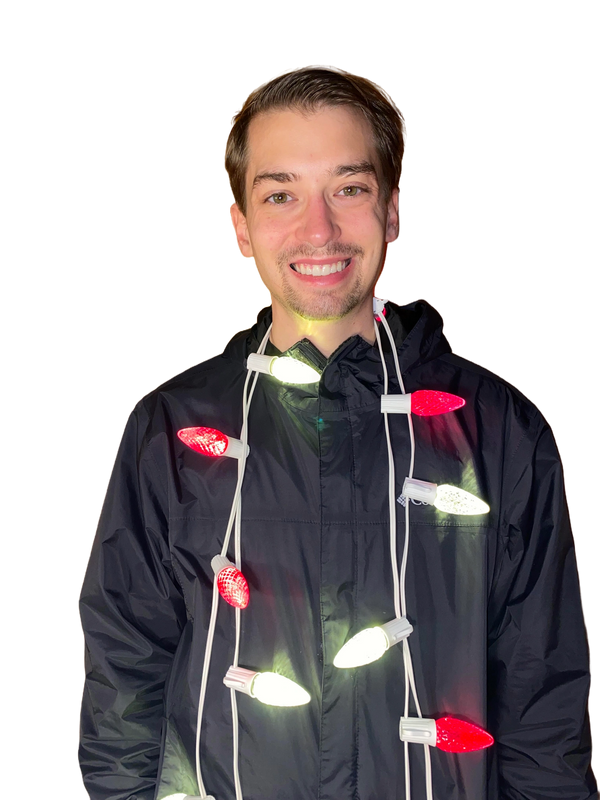 Smiling man wearing a black jacket with red and white Christmas lights around his neck.