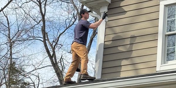 A man painting the exterior siding of a house while standing on the roof.