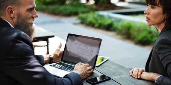 Two professionals discussing a project using a laptop outdoors.