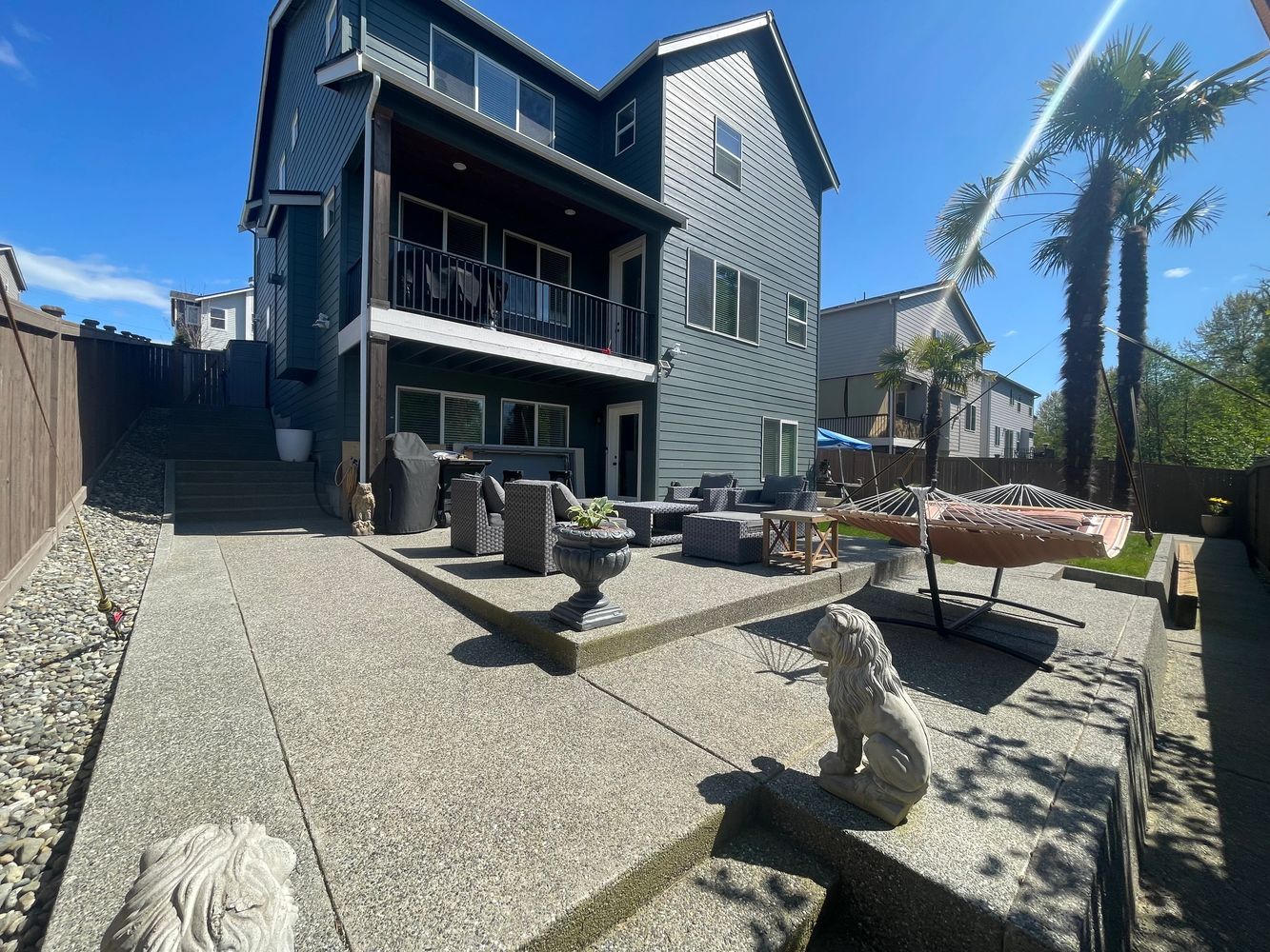 Modern backyard patio with seating, hammock, and palm trees under a clear sky.