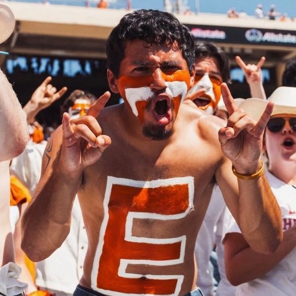 Excited fan with face and chest painted in orange and white at a sports event.