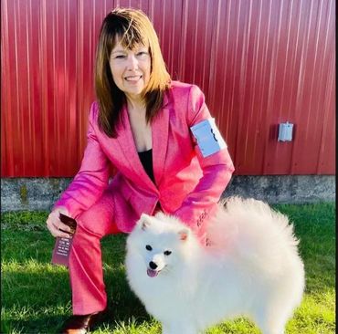Woman in pink suit with fluffy white dog outdoors.