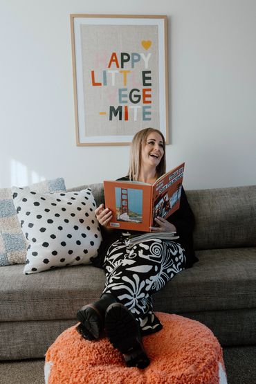 Karla McCullum laughing, sitting reading a book. Photography by THESE ARE THE DAYS PHOTOGRAPHY.