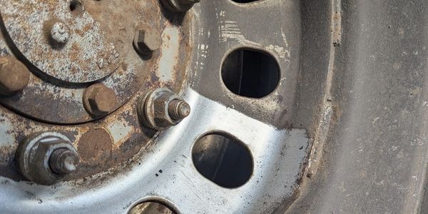 Close-up of a rusty vehicle wheel rim with nuts and bolts.
