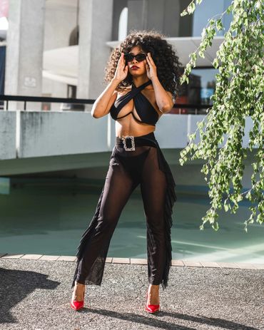 stylish girl with natural black hair poses in front of water while wearing fashion outfit