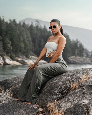 girl wearing vacation fashion sits on rock along the beach on the west coast with forrest behind her