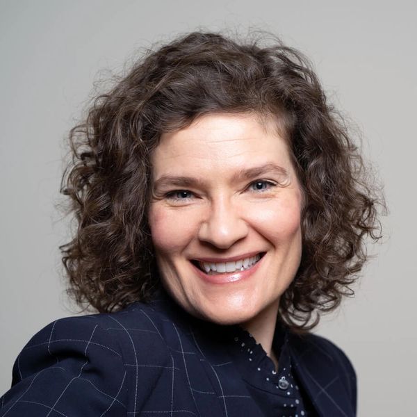 Smiling woman with curly hair in a dark checked blazer.