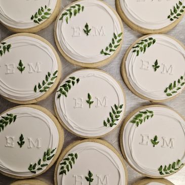 Elegant round cookies with white icing and green leaf designs, embossed with initials E and M.