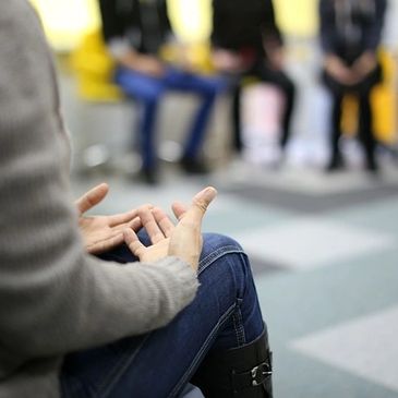 A person with open hands in their lap in a group therapy setting.