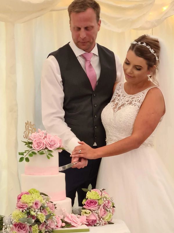 A bride and groom cut the wedding cake. The 3-tier cake is topped with sugar flowers