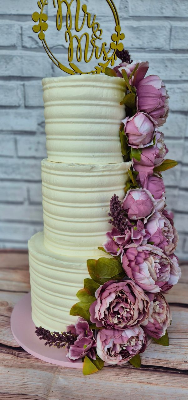 3-tier wedding cake covered in thick buttercream with a textured pattern and a band of silk peonies