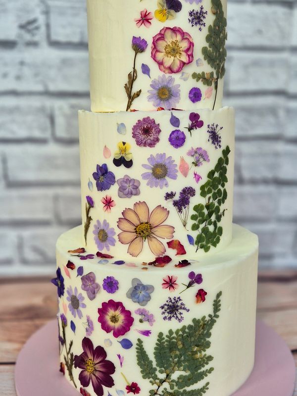 a 3-tier wedding cake covered in buttercream with a band of dried edible pressed flowers
