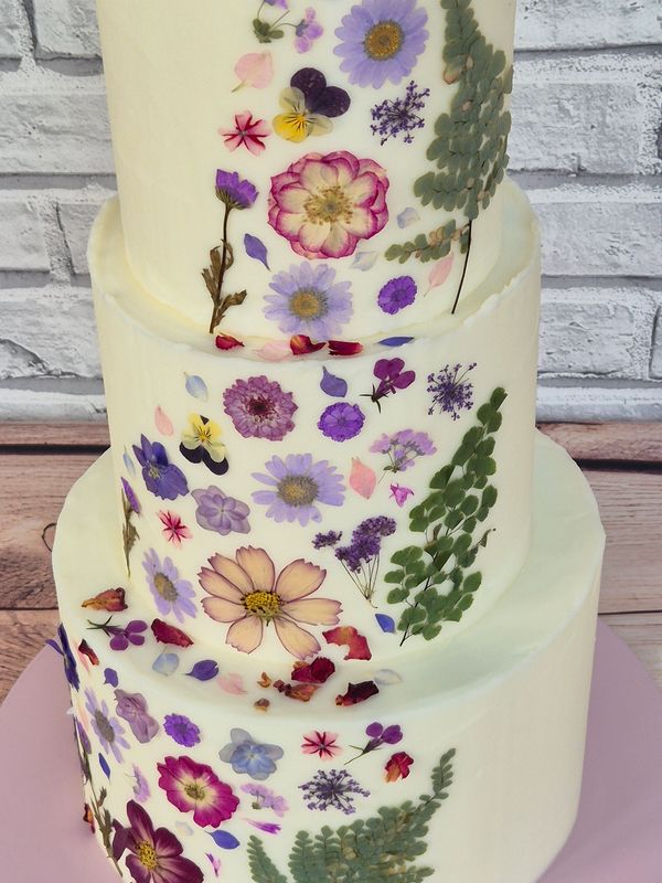 a 3-tier wedding cake covered in buttercream with a band of dried edible pressed flowers