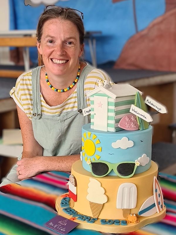 A perso sitting next to a large multi-tiered cake with a beach theme.