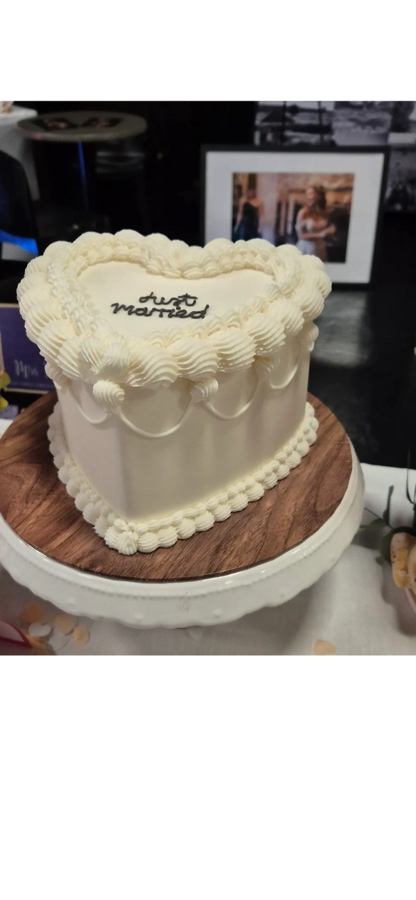 A heart-shaped wedding cake with white icing and piped edges sits on a cake stand.