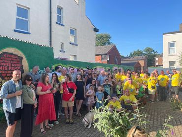A photo of Sam's family and friends celebrating his birthday, all stood in front of the mural.