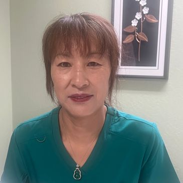 Woman with auburn hair wearing a teal top and pendant necklace.