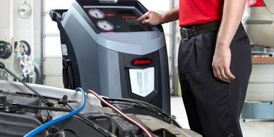 Technician operates a diagnostic machine on a car engine in a garage.
