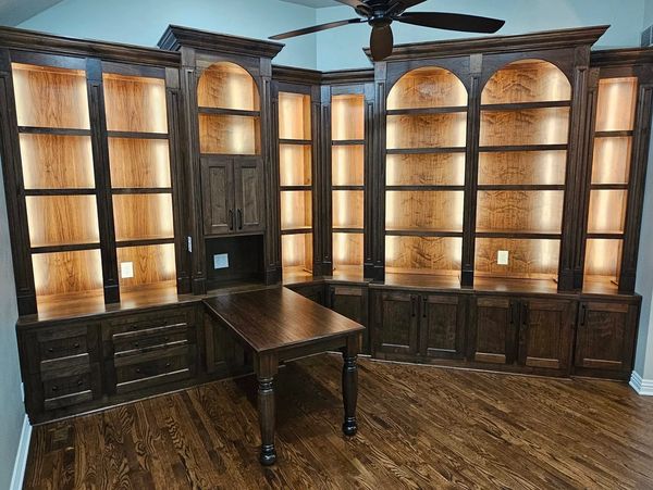 Elegant dark wood built-in shelves with warm backlighting and a matching table in a corner room.