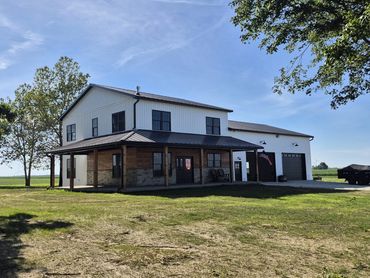 Two-story white board-and-batten farmhouse with a stone-wrapped covered porch and attached garage