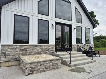 Modern farmhouse entry with tall black-framed windows, stone base and concrete steps