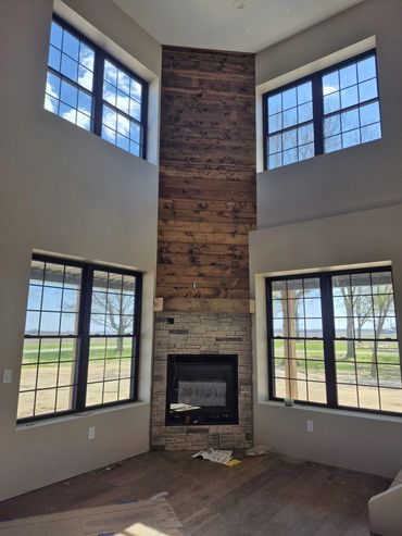 Two-story great room with a reclaimed-wood fireplace wall between tall black windows