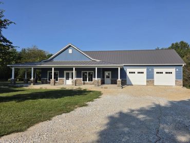Blue ranch home with a full-length covered porch, stone accents and a two-car garage