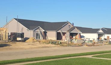 Row of tan and gray duplex condos with gabled entries, near completion