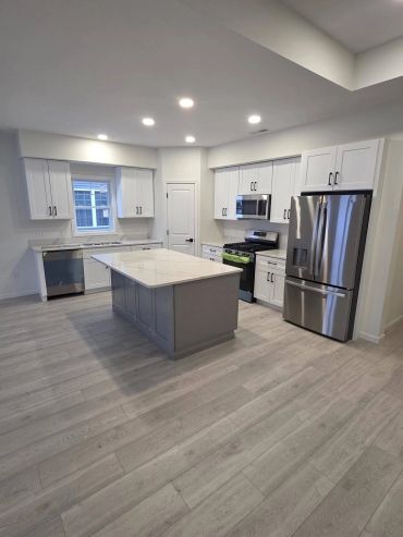 Condo kitchen with white cabinets, gray island, light countertops and stainless appliances