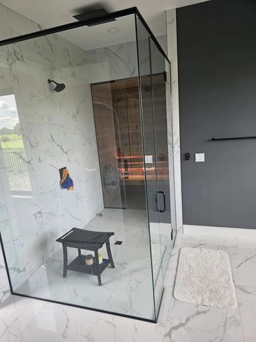 Walk-in glass shower with marble-look tile and black fixtures