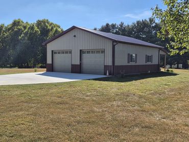 Gray steel-sided garage with two white overhead doors and wainscot