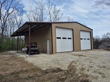Tan post-frame shop with two overhead doors and a covered lean-to