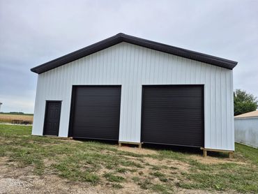 White post-frame shop with two black overhead doors and a black walk door
