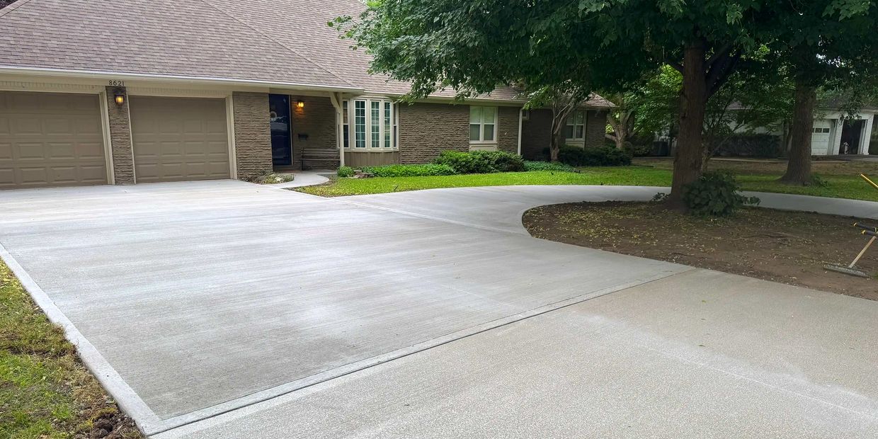 Newly poured concrete driveway in front of a suburban house with a large tree.