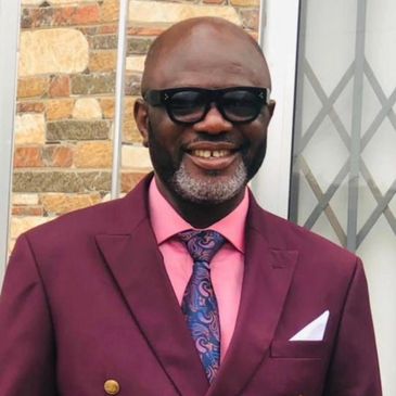 Dr. Joseph Obeng is shown in a full color photograph with a wine-colored suit and pink shirt.