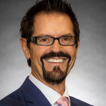 Mr. Tim Novak is shown in his blue suit, dark brown hair, and a white shirt with pink tie.