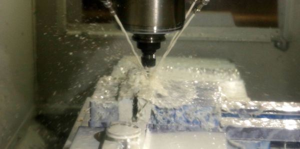 A CNC Machine cutting a part that is held in a vise. Coolant is spraying on the part. 