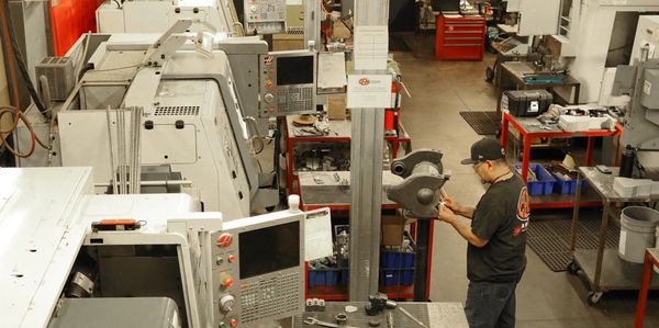 An employee operating next to three CNC Lathes and three CNC Mills. 