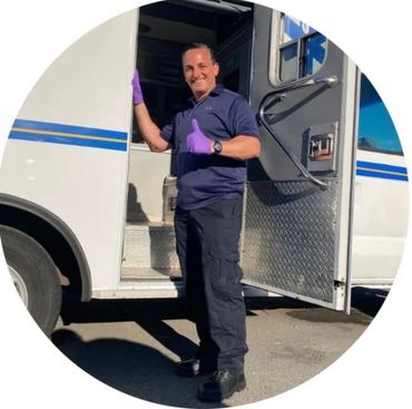 Smiling man in uniform giving thumbs up by an open vehicle door.