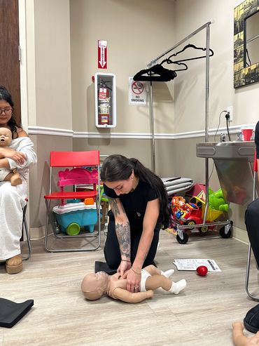 Woman practices infant CPR on a dummy in a training room.
