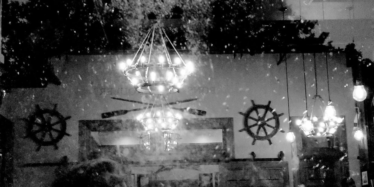 Reflection of chandeliers and streetlights on a rainy window at night.