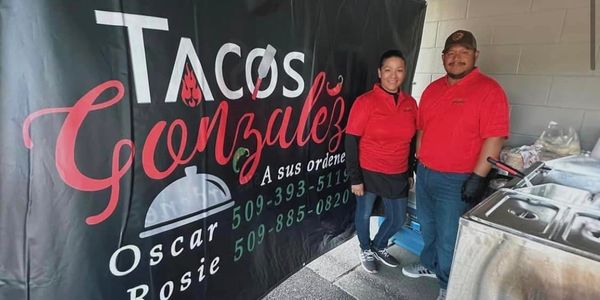 Tacos Gonzalez team under a tent next to a cooking station with branded banner in the background.