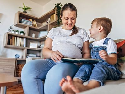 Pregnant woman reading a book with a young boy on a couch.