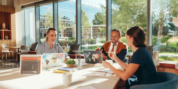 Three colleagues collaborating in a sunny, modern office with laptops and notebooks.