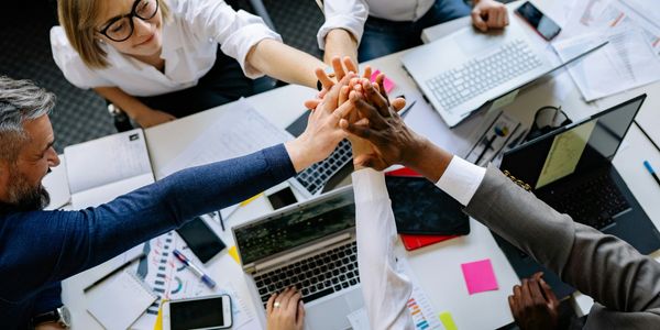 Diverse team celebrating success with a group high-five over a cluttered workspace.